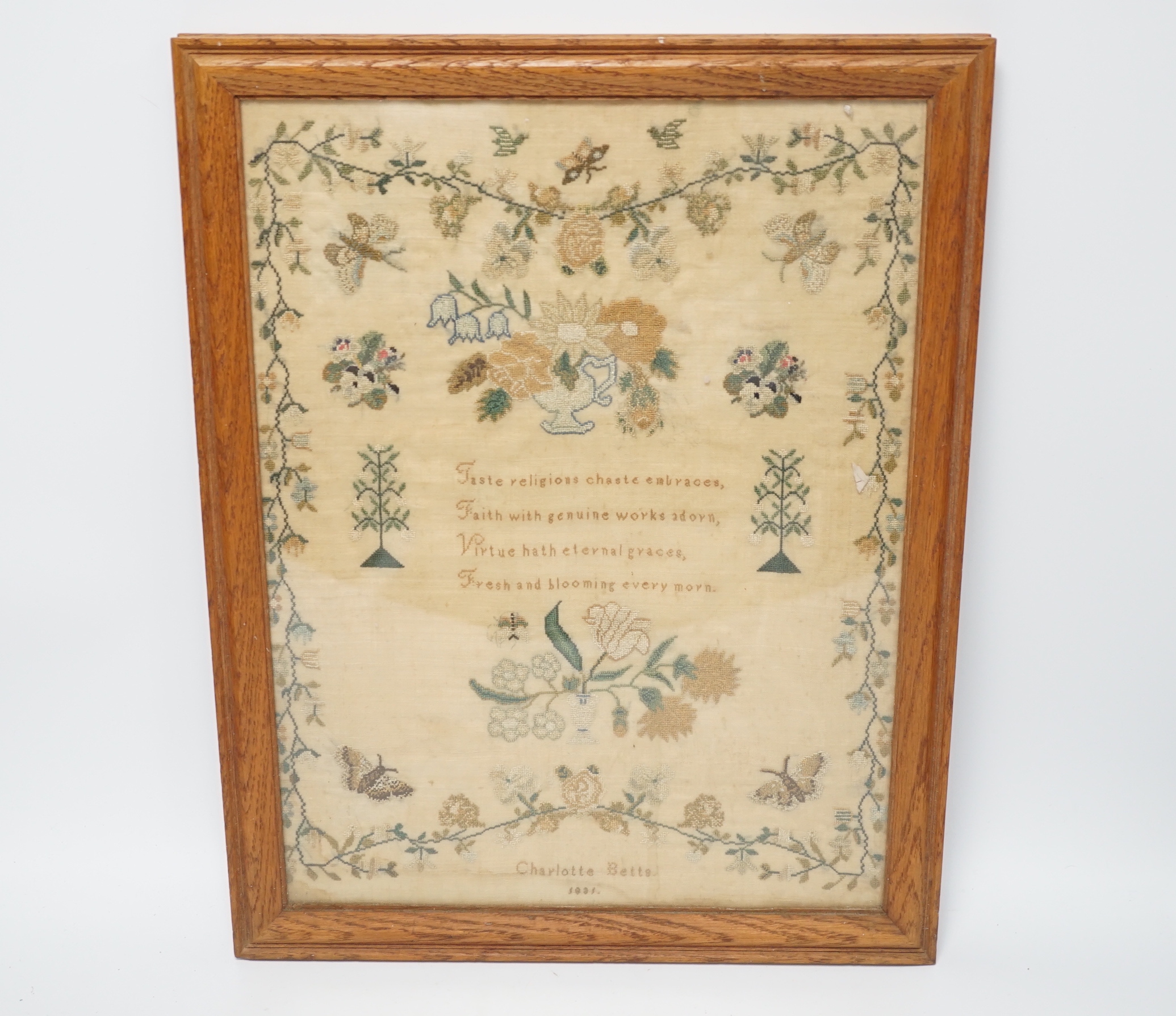 A framed sampler by Charlotte Betts, dated 1831, embroidered with a central religious verse, scrolling flowers, butterflies and birds, overall 45cm x 35cm